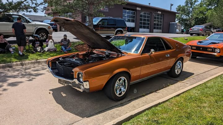 Orange classic car at an outdoor gathering, shared in the Ozark Mountain Muffler Facebook group